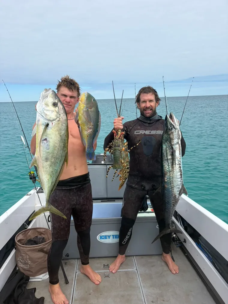 Two anglers on a boat holding fish and a crayfish after a day on the water